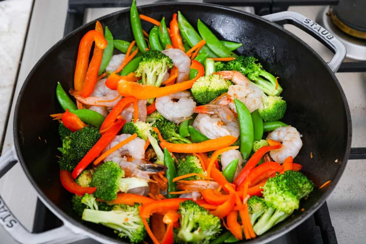 Shrimp added to the vegetables in wok. 