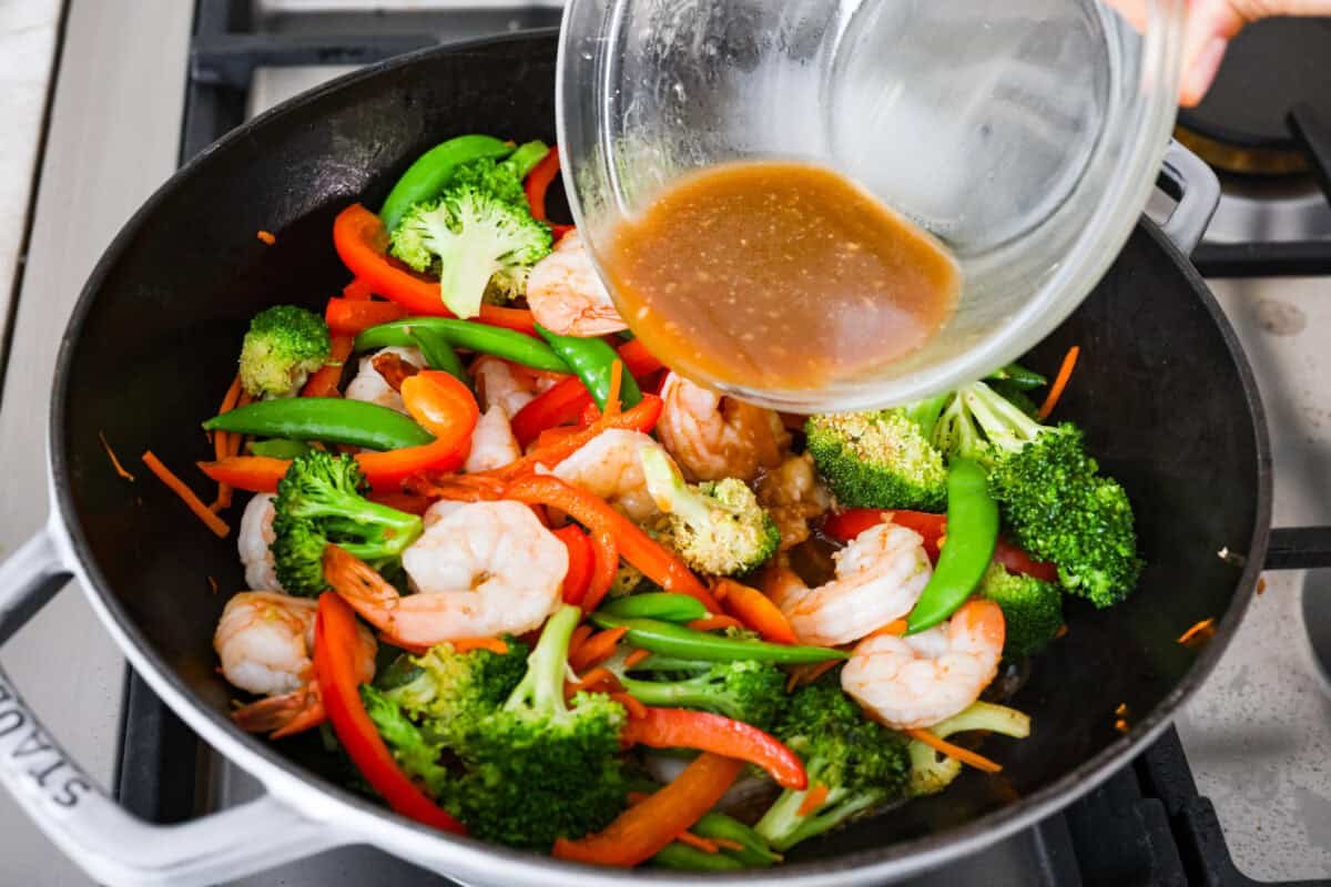 Garlic sauce is poured over shrimp and vegetables in wok. 